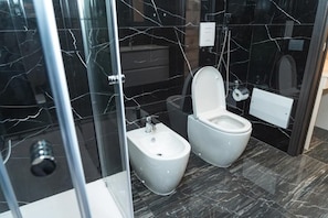A modern bathroom with a bidet, toilet, and glass shower enclosure. - Relais Mermaid (Naples)