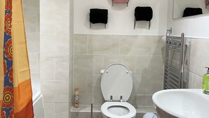 Une salle de bain moderne équipée de toilettes, d’un lavabo et d’une douche. On y trouve des serviettes et une poubelle.