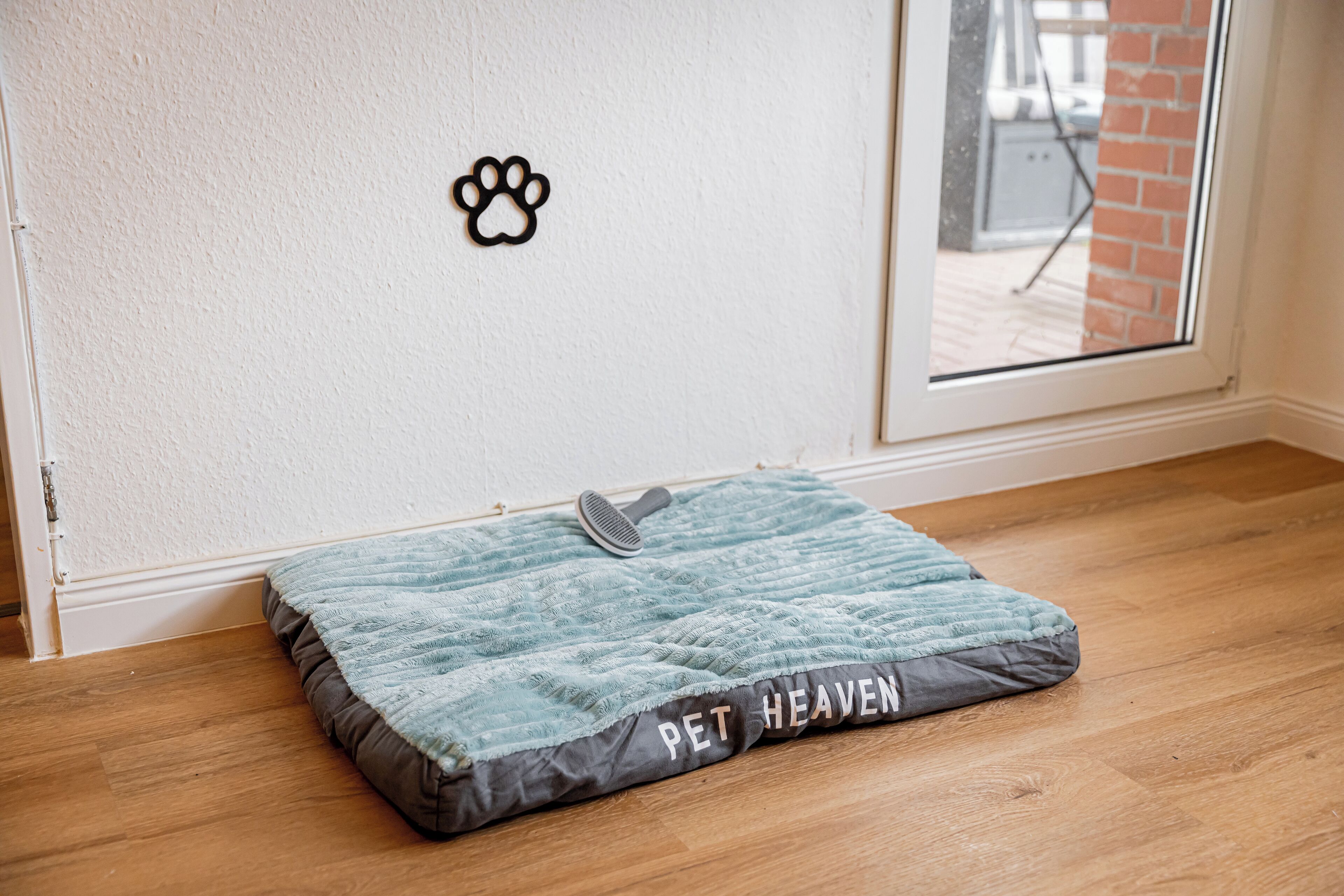 A pet bed labeled "PET HEAVEN" on a wooden floor near a white wall with a pet paw print decoration.