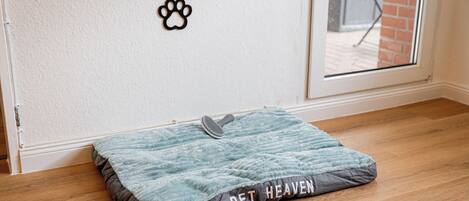 A pet bed labeled "PET HEAVEN" on a wooden floor near a white wall with a pet paw print decoration.