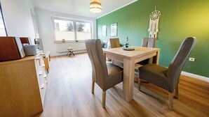 A dining area with a wooden table and chairs, a hanging light fixture, and a green accent wall.