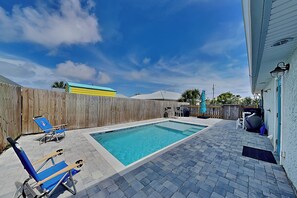A rectangular swimming pool with a tiled deck, two blue lounge chairs, and a wooden fence in the background. - A Stone's Throw | Pet Friendly, 2 Blocks to Beach, Large Yard (Panama City Beach)