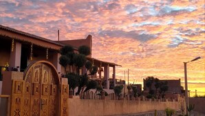 A traditional building with a large ornate wooden gate, a stone wall, and a well-maintained garden with various plants. - Villa Calm, Panoramic View of the Lake and Mountains, Ouarzazate Center (Ouarzazate)