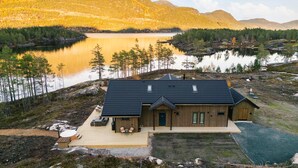 Une cabane dotée d’une terrasse, d’un petit espace extérieur aménagé pour s’asseoir, et offrant une vue sur un lac et des montagnes boisées.