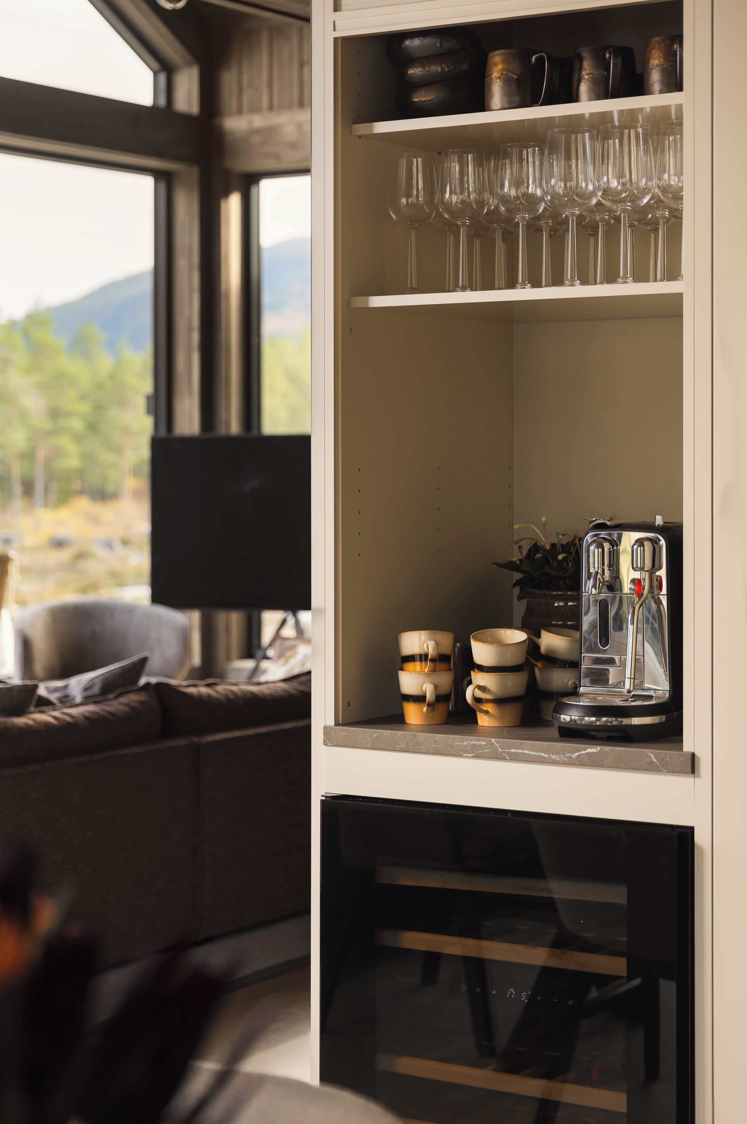 Una habitación con un sofá, una cafetera y un estante con cristaler ía y tazas.