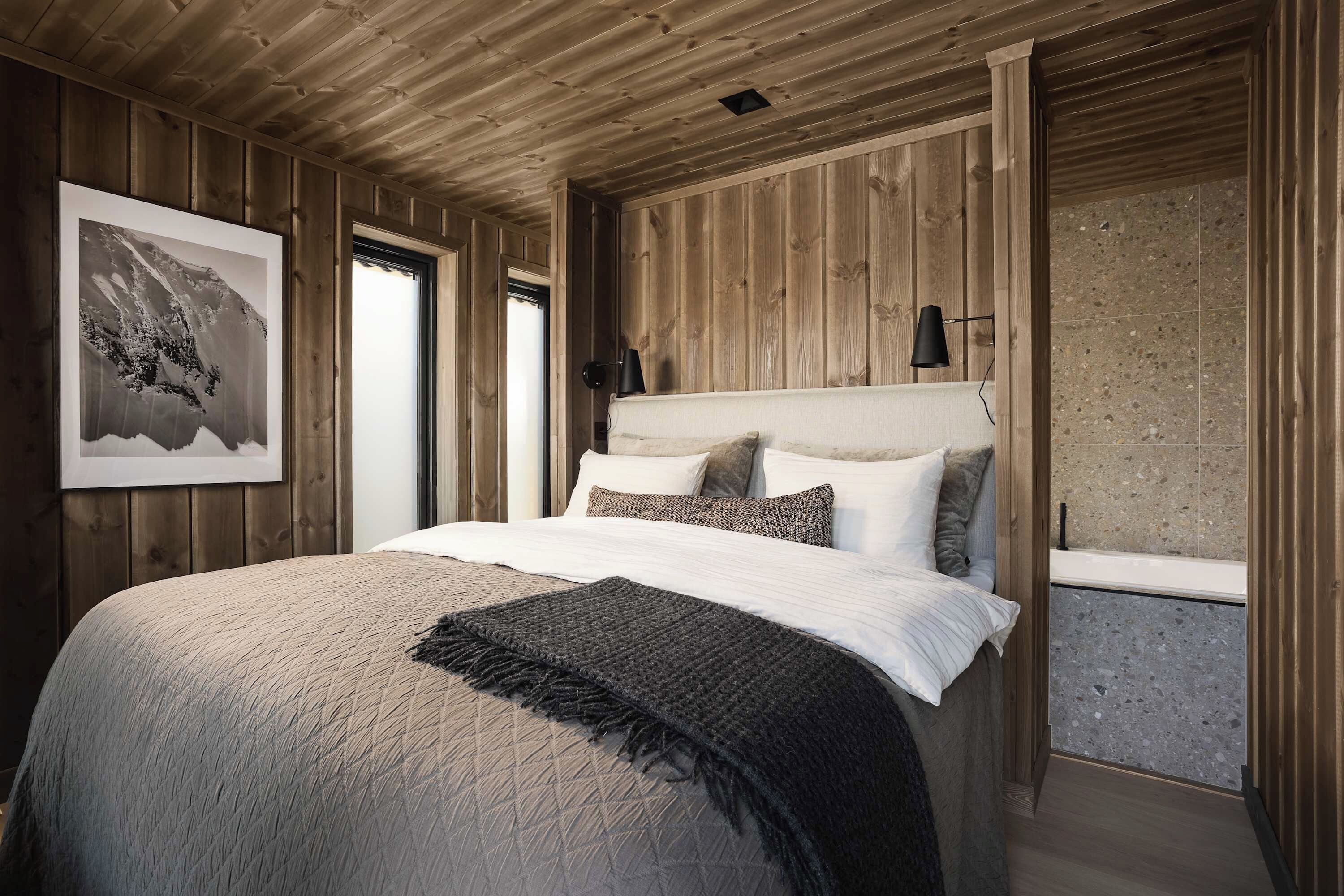 Un dormitorio con paneles de madera, una cama, almohadas, un plaid y un cuadro en la pared.