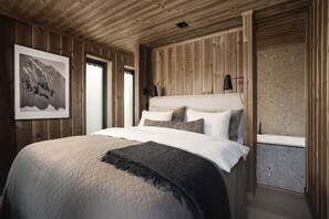Un dormitorio con paneles de madera, una cama, almohadas, un plaid y un cuadro en la pared.