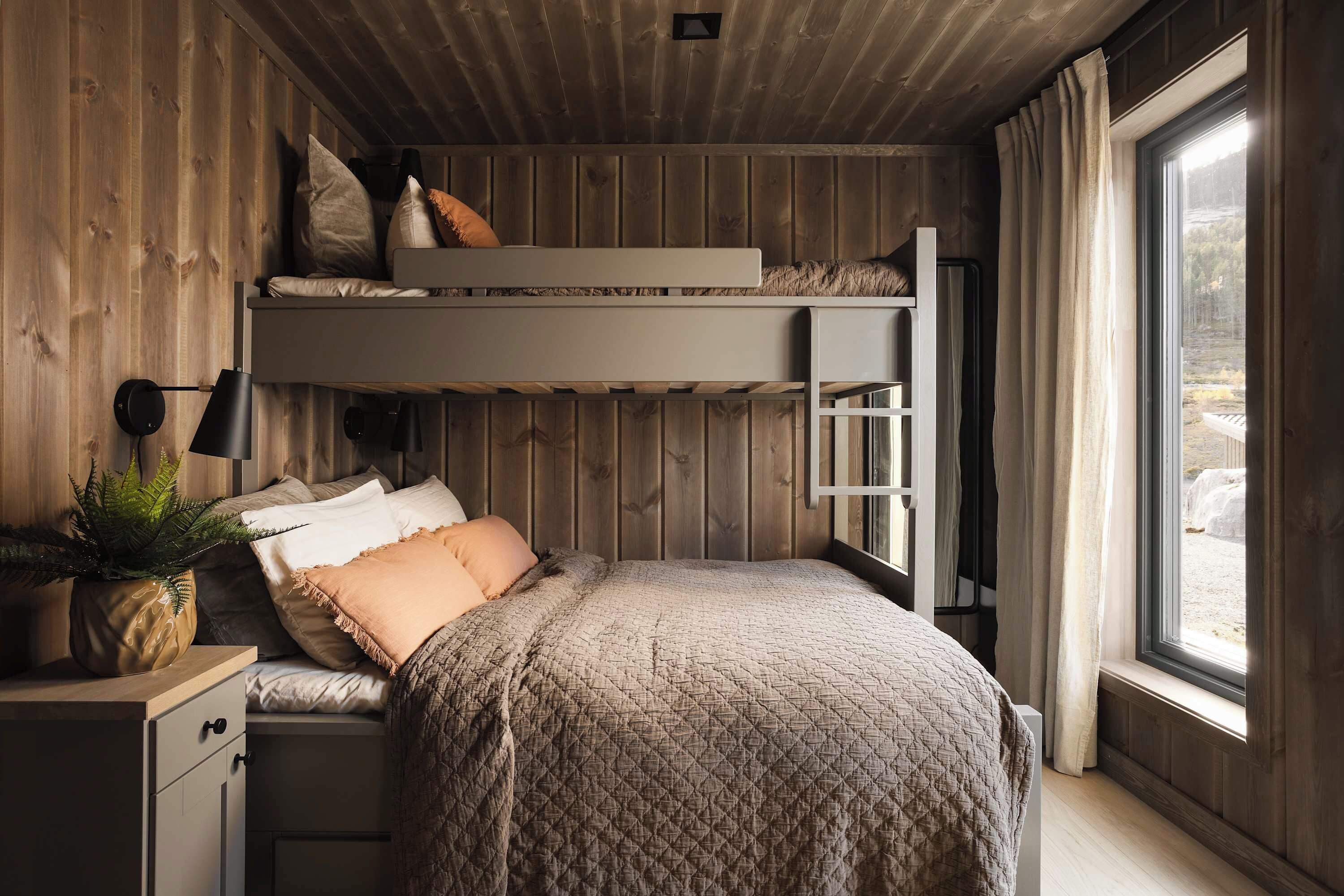 Habitación con literas, un escritorio, una planta en maceta y una ventana con cortinas.