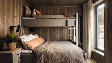 A bunk bed room with a desk, a potted plant, and a window with curtains.