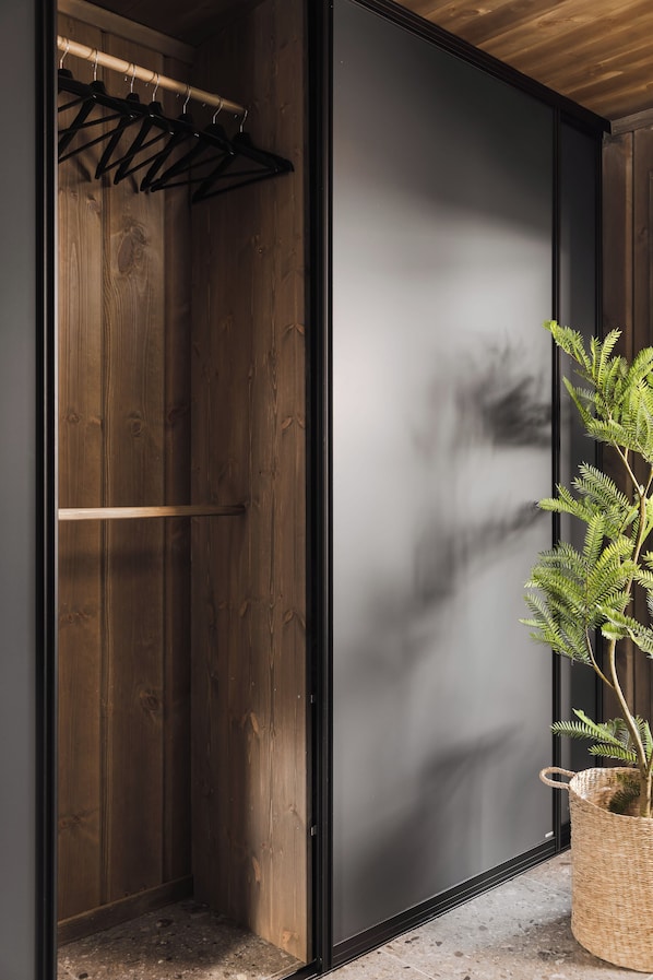 Una habitación con un armario de madera, perchero y una planta en maceta.