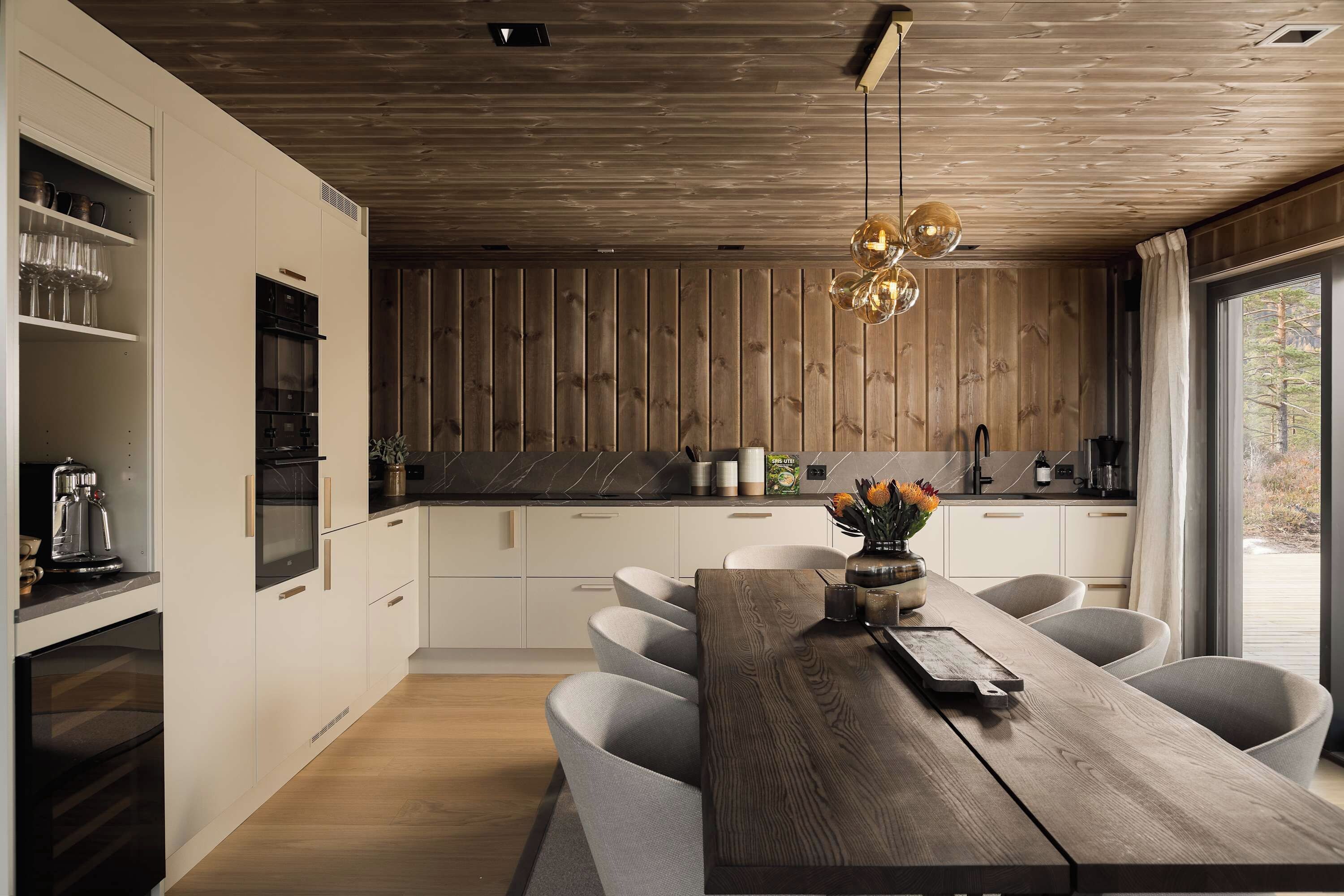 A modern kitchen with wooden paneling, a dining area with a wooden table, and a view of the outdoors.