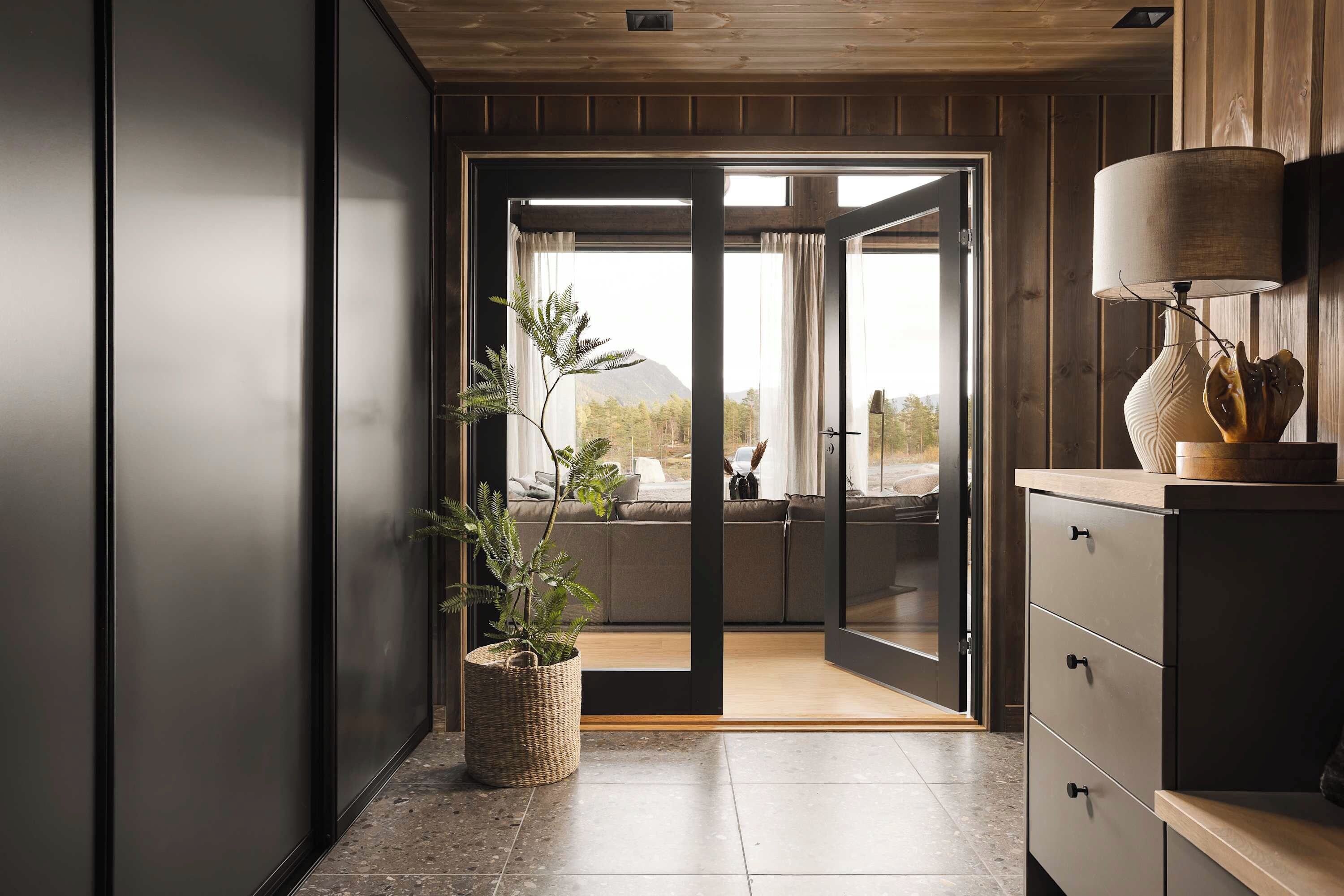 Een modern interieur met een schuifglazen deur naar een balkon, een potplant en een houten kast met een lamp.
