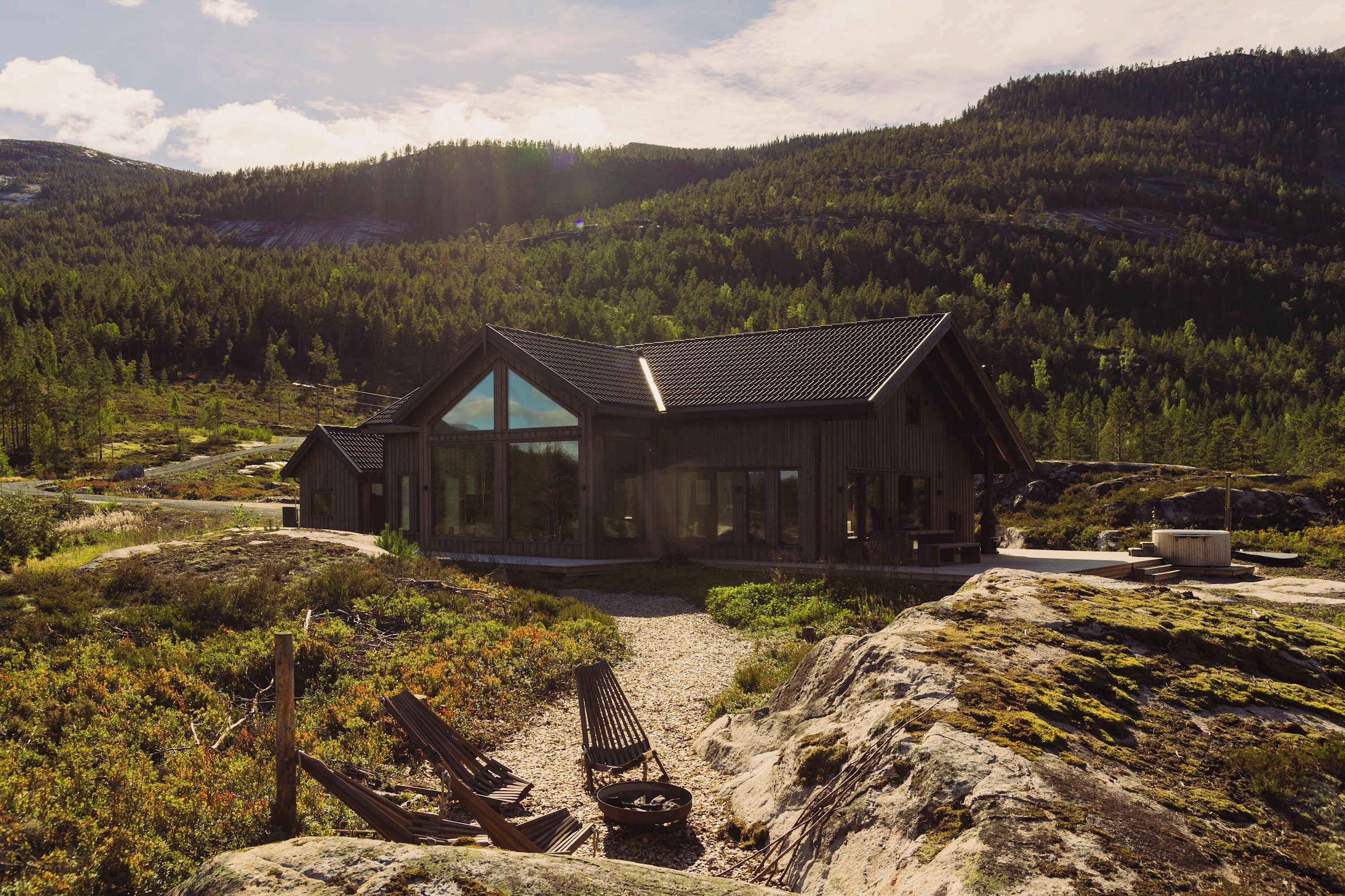 A wooden cabin with a sloped roof, large windows, and a gravel driveway leading to it.
