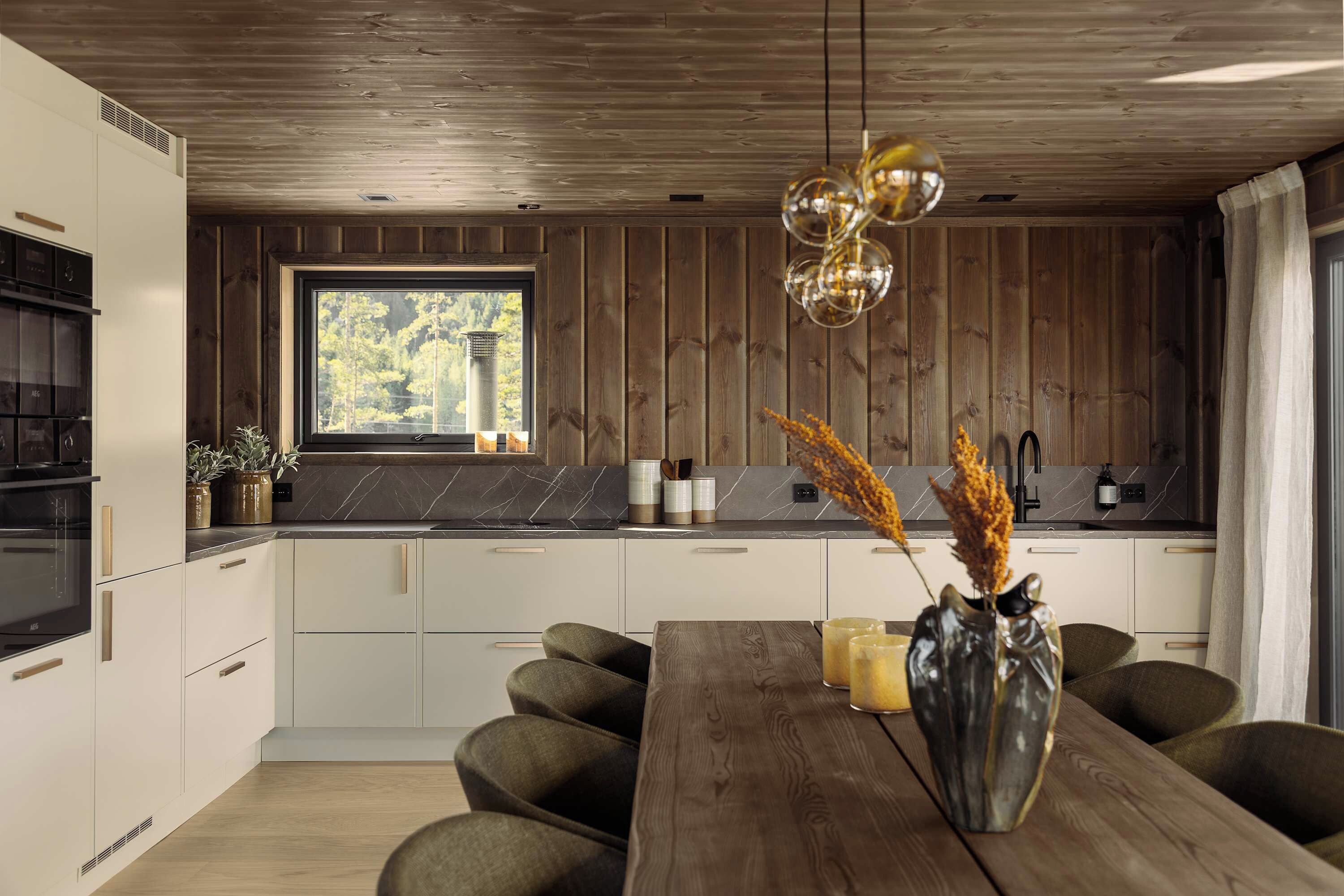 Una cocina moderna con techo de madera, una ventana con vista a árboles y un comedor con mesa y sillas.