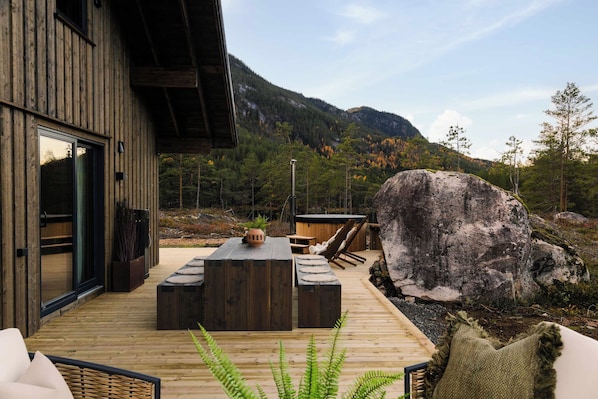 A wooden deck with outdoor furniture, a large rock, and a mountain view.