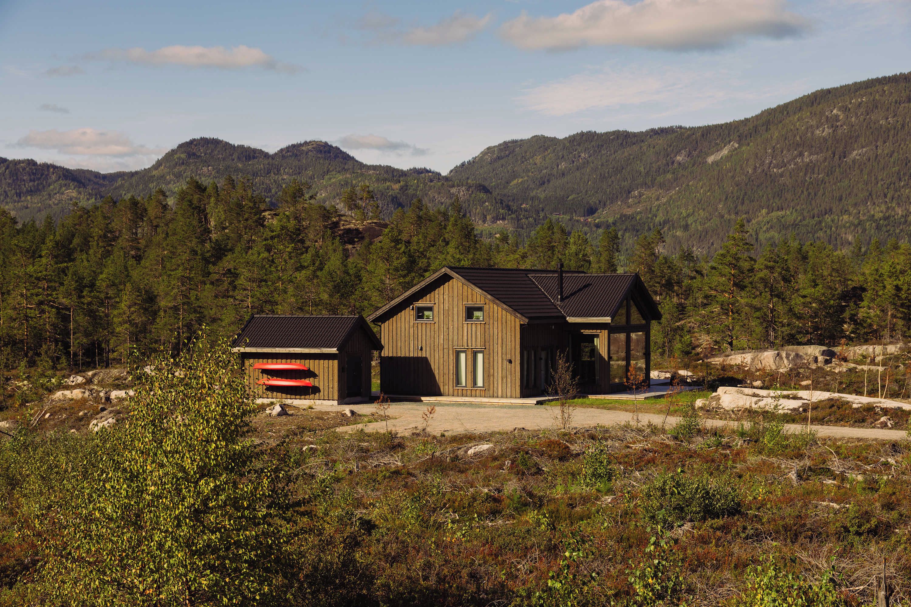 Une cabane avec un garage et une véranda couverte, entourée de montagnes boisées.