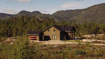 Une cabane avec un garage et une véranda couverte, entourée de montagnes boisées.