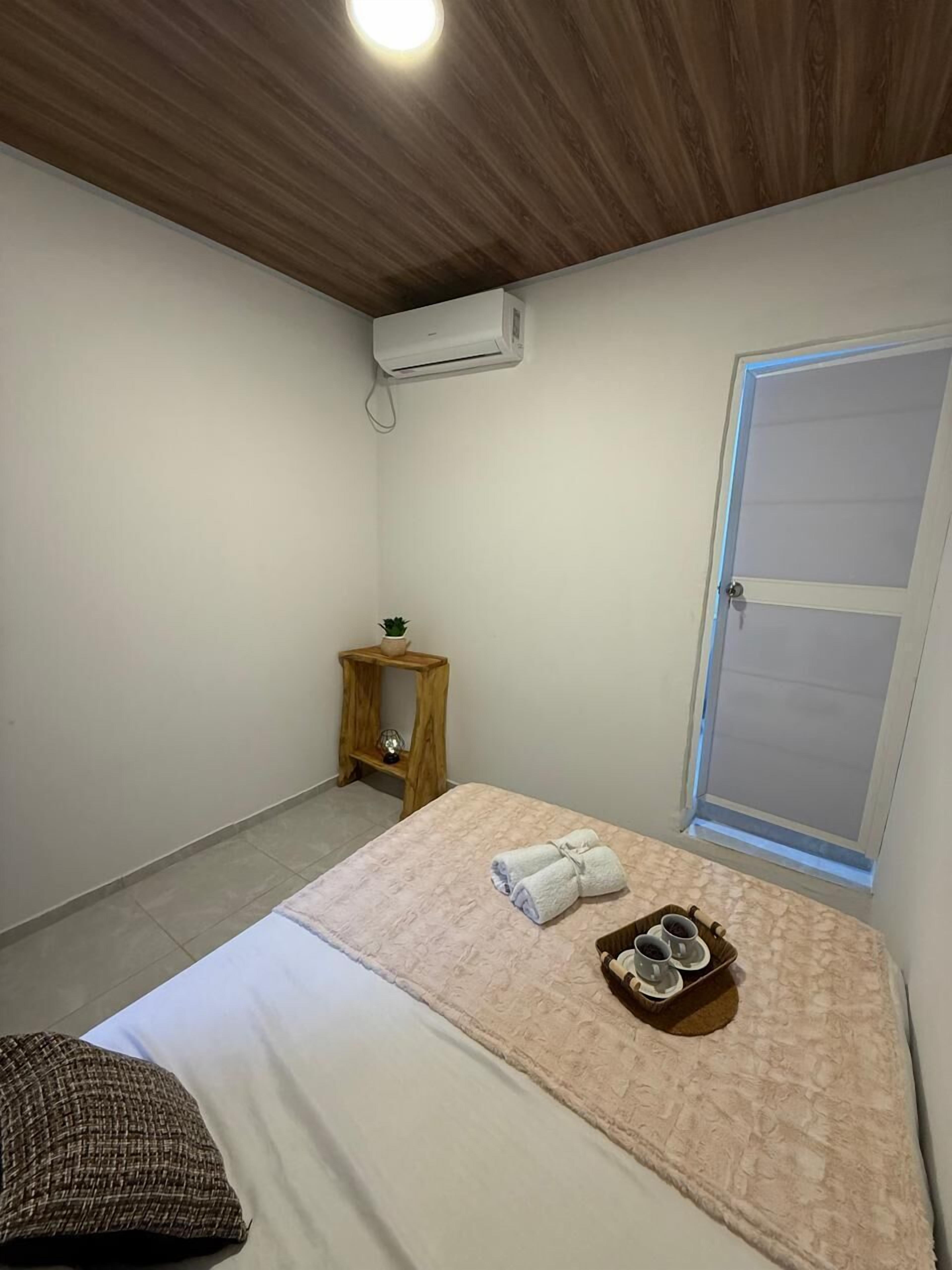 A bedroom with a bed, a small wooden side table, a towel, and a tray with cups.