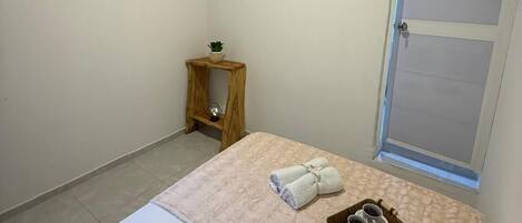A bedroom with a bed, a small wooden side table, a towel, and a tray with cups.