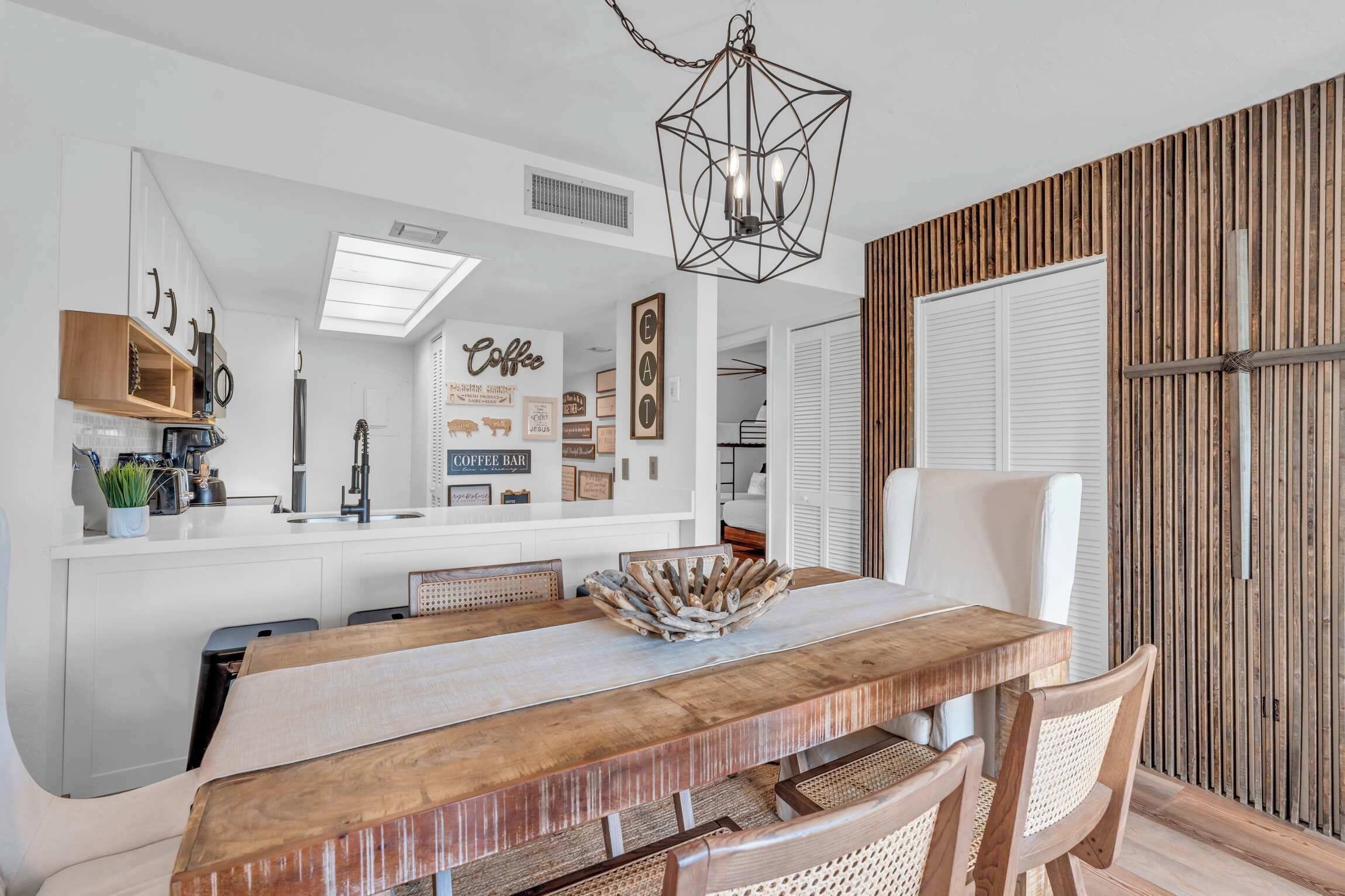 A modern kitchen with white cabinetry, a coffee bar, and a dining area with a wooden table and chairs.