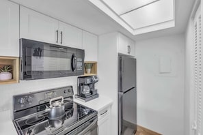 Eine moderne Küche mit weißen Schränken, einem Edelstahlkühlschrank, einer eingebauten Mikrowelle, einer Kaffeemaschine und einem Wasserkocher auf dem Herd.