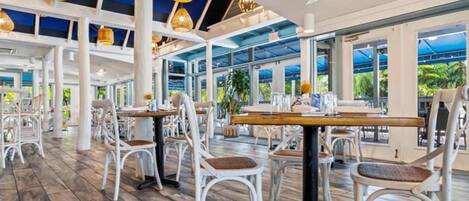 An indoor dining area with white chairs, tables, and a high ceiling with exposed beams.