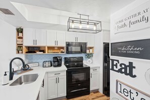 A modern kitchen with white cabinets, a black stove, and a sign that says "Come gather at faith, family." - G-243 - Spend Your Vacation in Luxury with Pool (Naples)