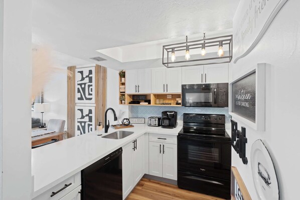 A modern kitchen with white cabinetry, a black stove, and a coffee maker. - G-243 - Spend Your Vacation in Luxury with Pool (Naples)