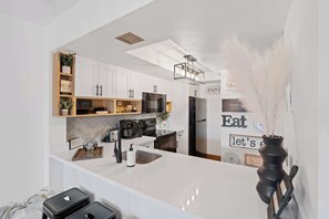 A modern kitchen with white cabinets, a black refrigerator, and a white countertop. There is a black vase with white feathers on the counter. - G-243 - Spend Your Vacation in Luxury with Pool (Naples)