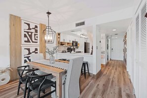 A modern kitchen with white cabinets, a central island, and a dining area with a wooden table and black chairs.