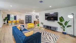 A modern living room with a blue sofa, yellow chairs, a TV, and a fireplace. - 5-BD Modern Central Getaway w Hot Tub - Mins to DT (Houston)