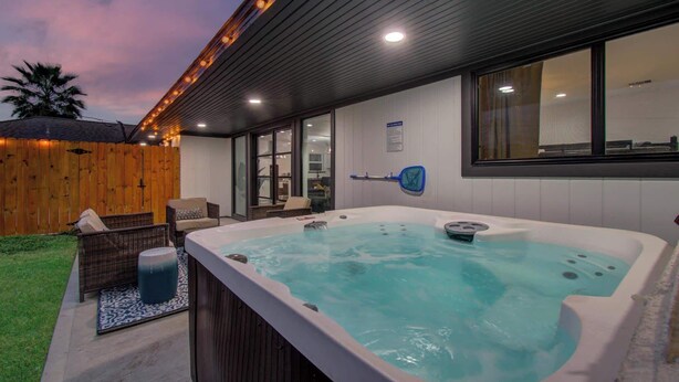 A hot tub with a wooden deck and chairs, a wooden fence, and a window with a safety sign. - 5-BD Modern Central Getaway w Hot Tub - Mins to DT (Houston)