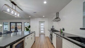 A modern kitchen with a central island, stainless steel appliances, and a view to the outside. - 5-BD Modern Central Getaway w Hot Tub - Mins to DT (Houston)