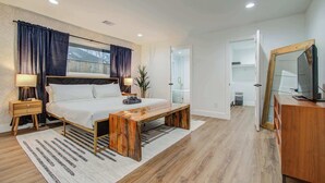 A modern bedroom with a large bed, bedside lamps, a wooden bench, and a walk-in closet. - 5-BD Modern Central Getaway w Hot Tub - Mins to DT (Houston)