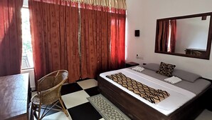 Ein Hotelzimmer mit Schachbrettmuster-Boden, einem Bett mit gemusterten Betttextilien, einem Sessel, einem Schreibtisch und einem Deckenventilator.
