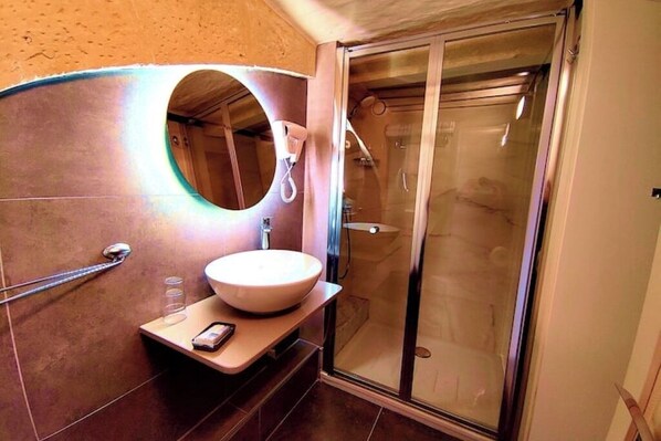 A bathroom with a round mirror, a sink, a handheld phone, and a glass-enclosed shower.