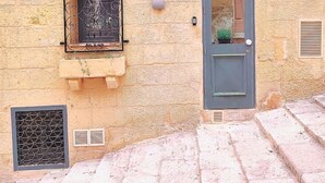 A stone building with a window with decorative iron bars, a door with a small window, and a ventilation grate.
