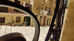 A courtyard with stone flooring, potted plants, and a building with balconies.