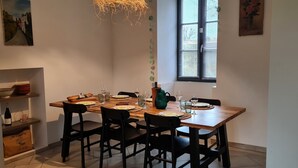 A dining area with a wooden table set for four, black chairs, a wine bottle, and a painting on the wall. - La Belle de Jard - 8 people (Jard-sur-Mer)