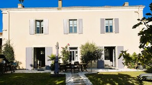 A two-story building with a central entrance, a covered patio area with tables and chairs, and a small garden with a pathway leading to the entrance. - La Belle de Jard - 8 people (Jard-sur-Mer)