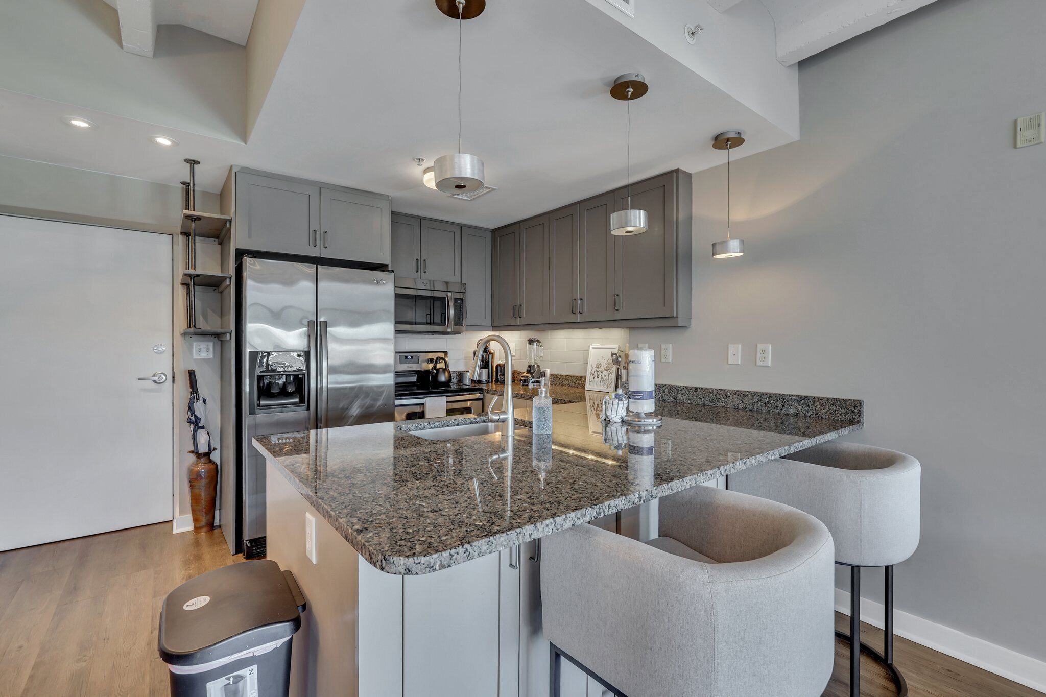 A modern kitchen with granite countertops, stainless steel appliances, and grey cabinetry.