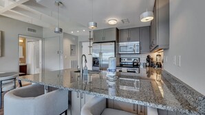 Una cocina moderna con encimeras de granito, electrodomésticos de acero inoxidable y una isla central con taburetes de bar.