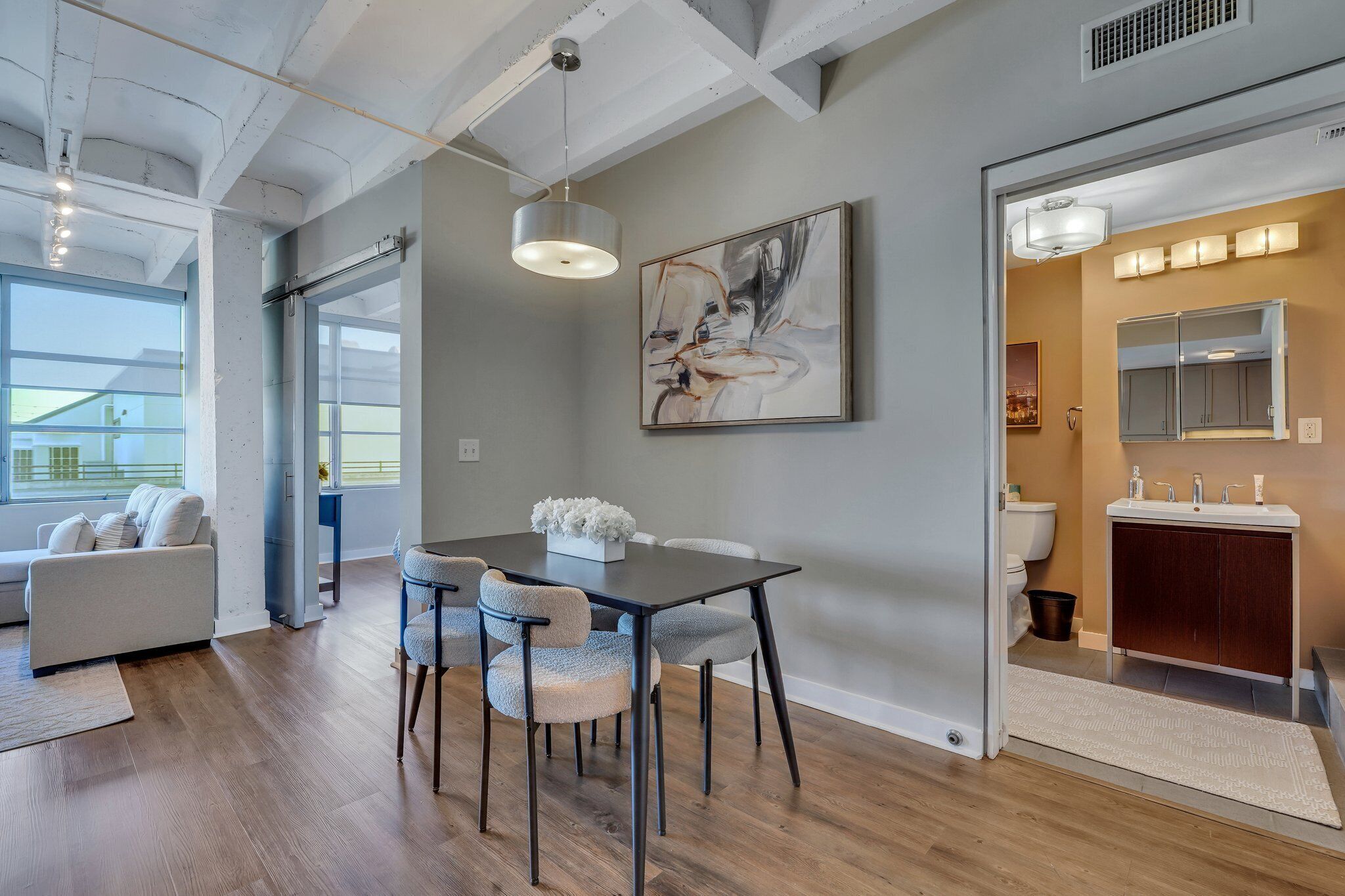 A modern interior with a dining area, a sofa, and a bathroom with a vanity and mirror.