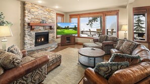 A living room with a stone fireplace, leather sofas, a television, and a view of a deck and trees. - Walk to the Winery & Chip onto the Par 3 Course! (Cle Elum)