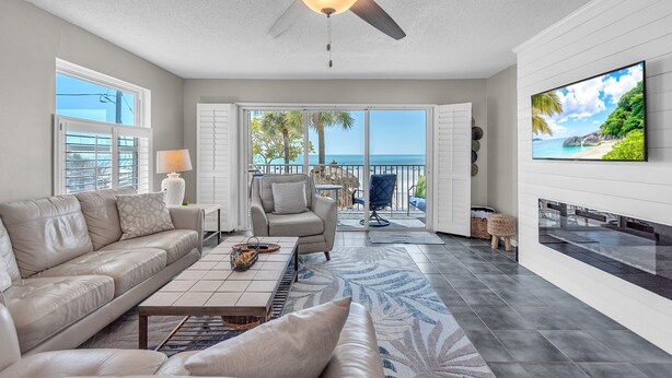 A spacious living room with a ceiling fan, a large TV, a sofa, and a view of the ocean through the sliding glass doors. - ☀️Beachfront with Great Views and Amenities-Sea Oats #101☀️ (Redington Shores)