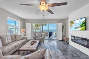 A spacious living room with a ceiling fan, a large TV, a sofa, and a view of the ocean through the sliding glass doors. - ☀️Beachfront with Great Views and Amenities-Sea Oats #101☀️ (Redington Shores)