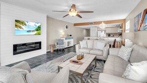 A modern living room with a fireplace, a large TV, and a ceiling fan. - ☀️Beachfront with Great Views and Amenities-Sea Oats #101☀️ (Redington Shores)