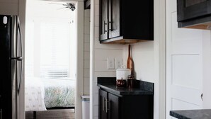 A kitchen with dark cabinets, a refrigerator, and a countertop with a kettle and mug. - Be Still Tiny House on Monteagle Mountain  (Tracy City)