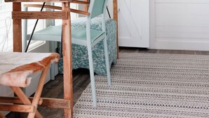 A room with a rustic wooden table, a light blue chair, a white door with a black handle, and a white wall with a black panel. - Be Still Tiny House on Monteagle Mountain  (Tracy City)