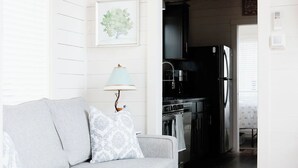 A living room with a grey sofa, a wooden bench, a lamp, and a framed picture on the wall. - Be Still Tiny House on Monteagle Mountain  (Tracy City)